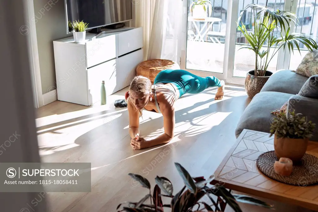 Woman practicing plank position while exercising on floor at home