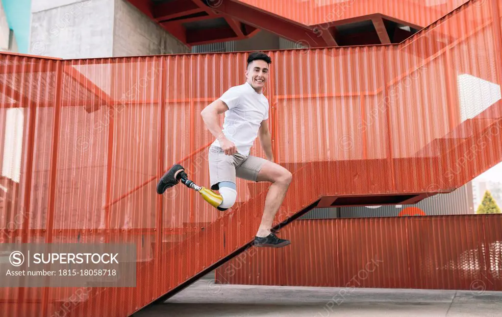 Young disabled man jumping against orange staircase