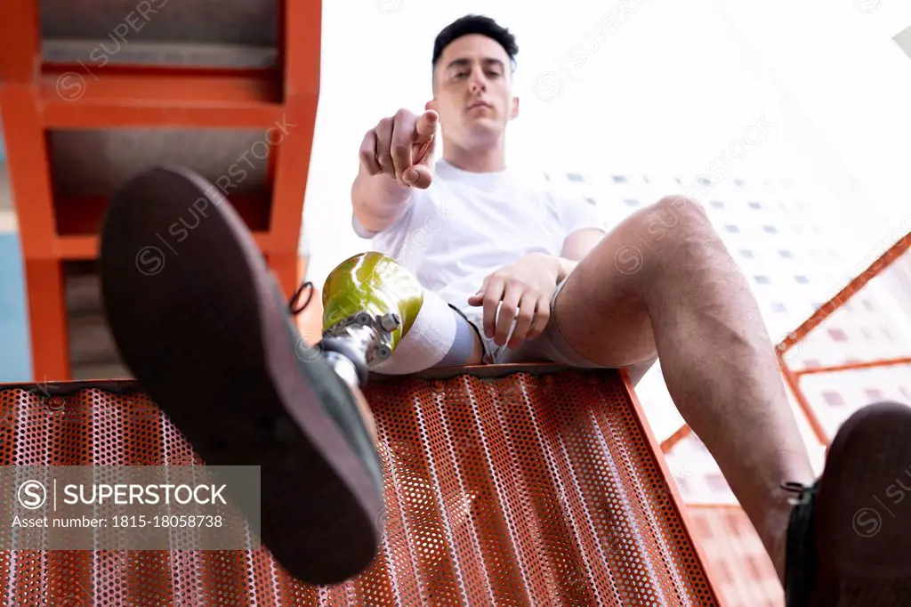 Amputated young man pointing while sitting on metal