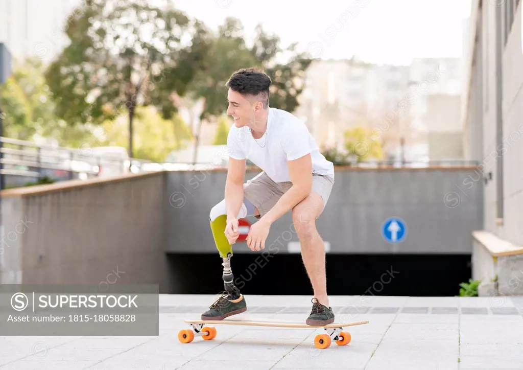 Smiling amputated man skateboarding against subway in city