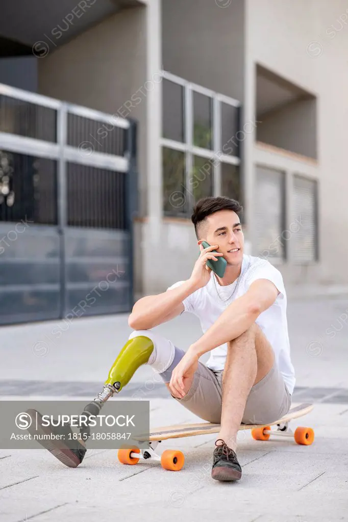 Young disabled man talking through mobile phone while sitting on skateboard