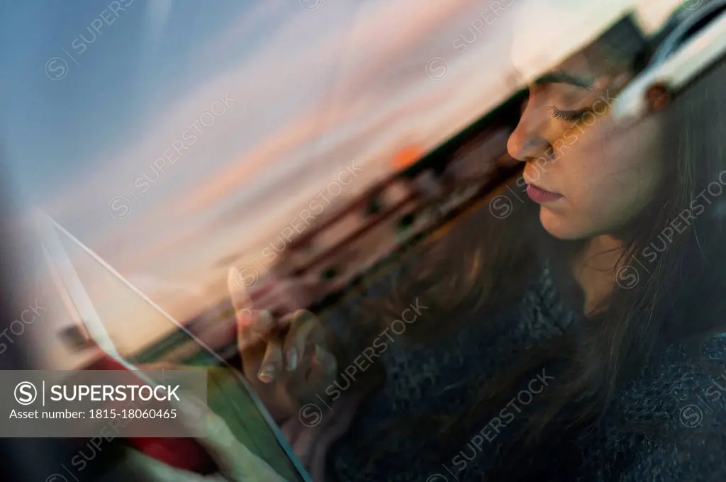 Young woman using digital tablet while travelling in car seen through glass window