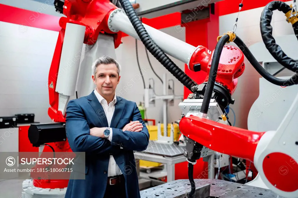 Male entrepreneur with arms crossed standing at robotics in factory