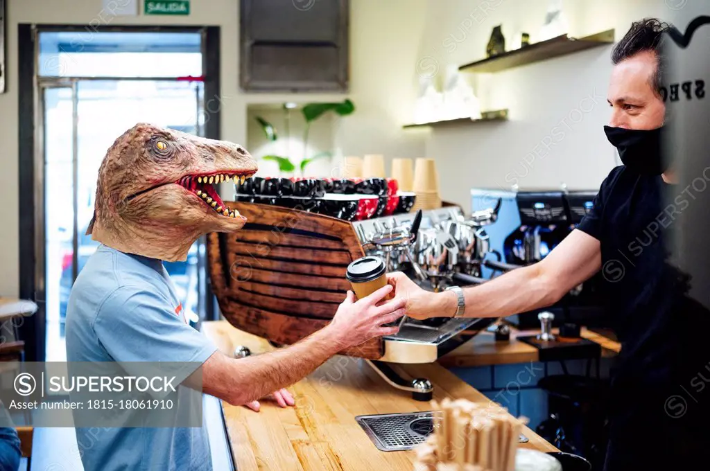 Man wearing dinosaur mask buying coffee from barista in cafe