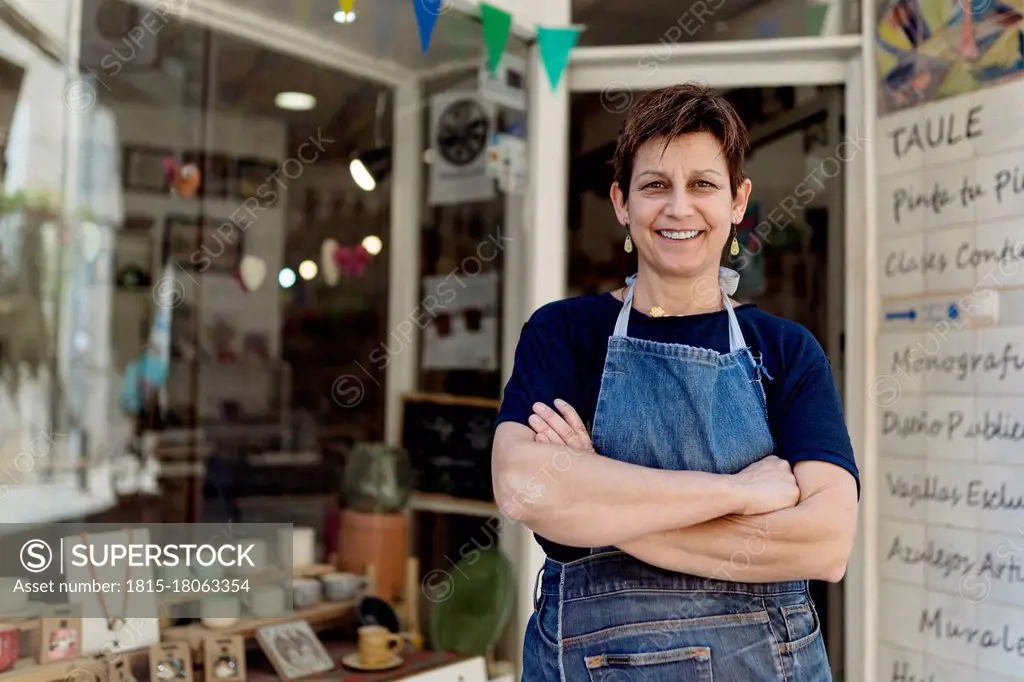 Happy small business owner standing with arms crossed outside her store