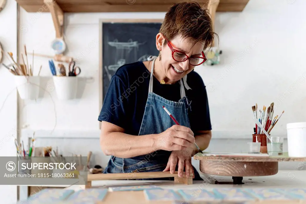 Smiling owner painting craft product in ceramic workshop