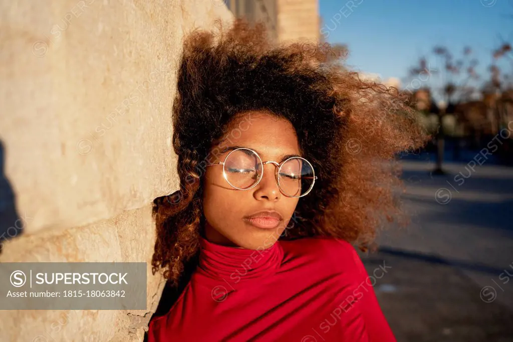 Young woman with eyes closed leaning on wall