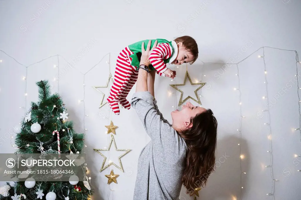 Smiling woman picking up baby boy while playing at home during Christmas