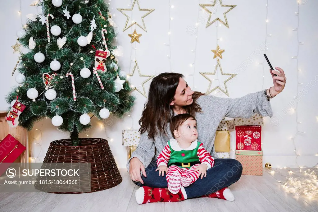 Mother taking selfie with son through mobile phone while sitting at home during Christmas