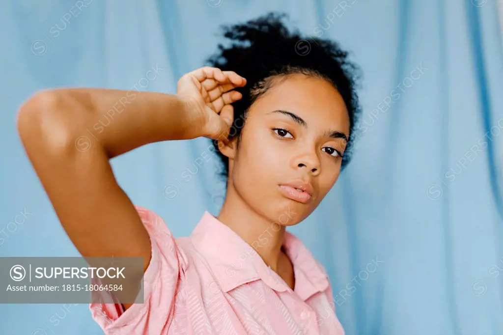 Contemplating woman with hand in hair against blue curtain