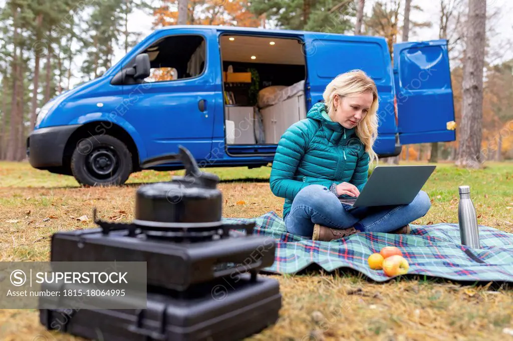 Woman working on laptop while sitting on picnic blanket at Cannock Chase