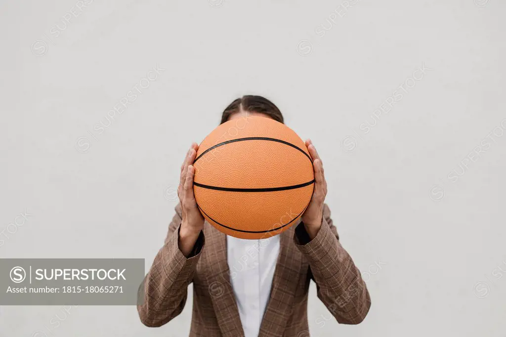 Female professional holding basketball in front of face against white wall