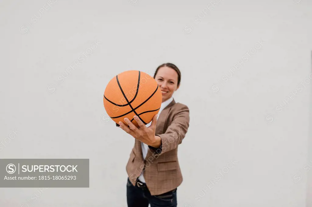 Playful female professional with basketball standing against white wall while taking break