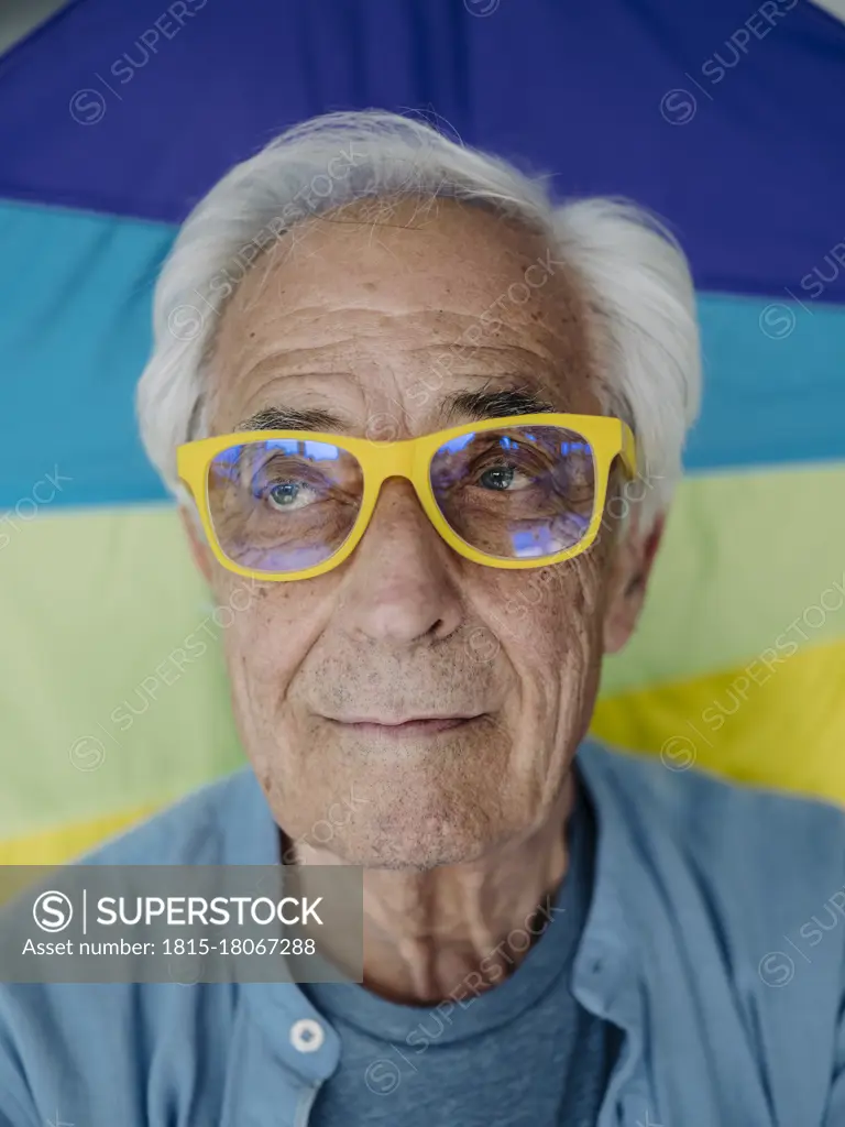 Businessman wearing yellow eyeglasses looking away while standing against multi colored wall