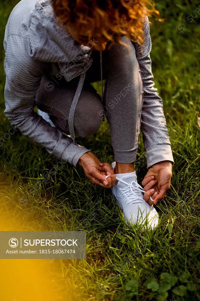 Female athlete tying shoelace while crouching at park