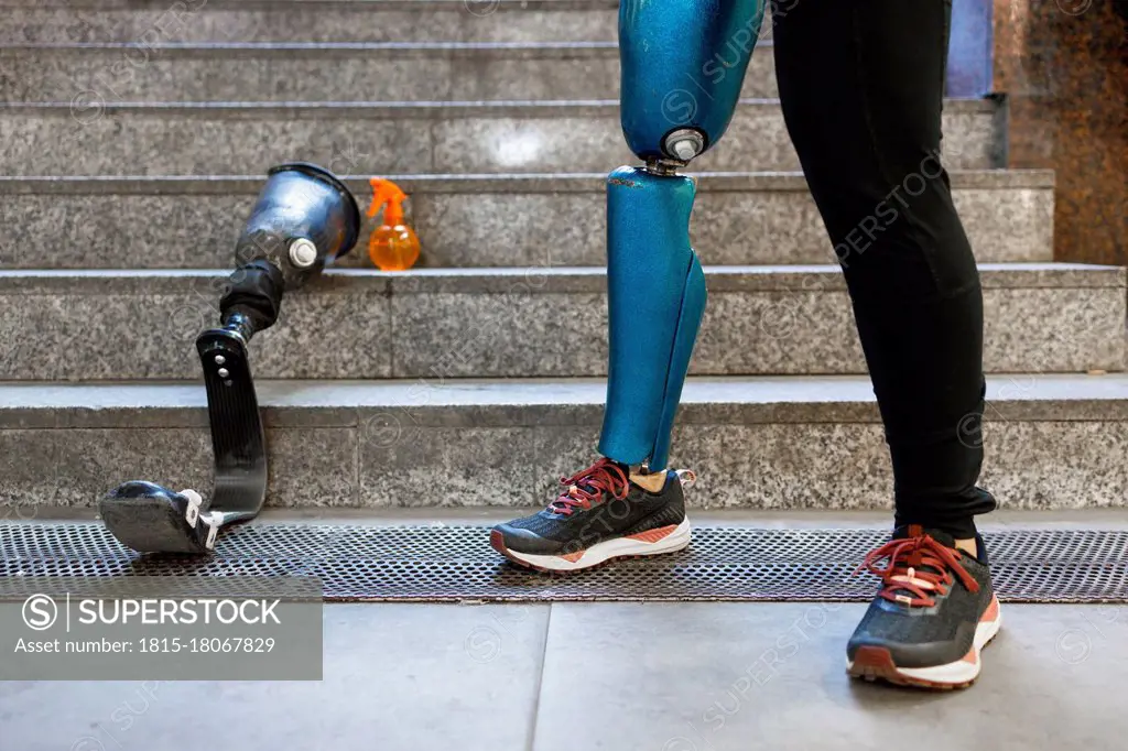 Young sportswoman with prosthetic leg standing by artificial limb on steps