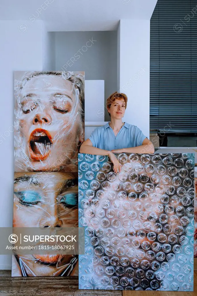 Smiling female artist standing with paintings in art studio