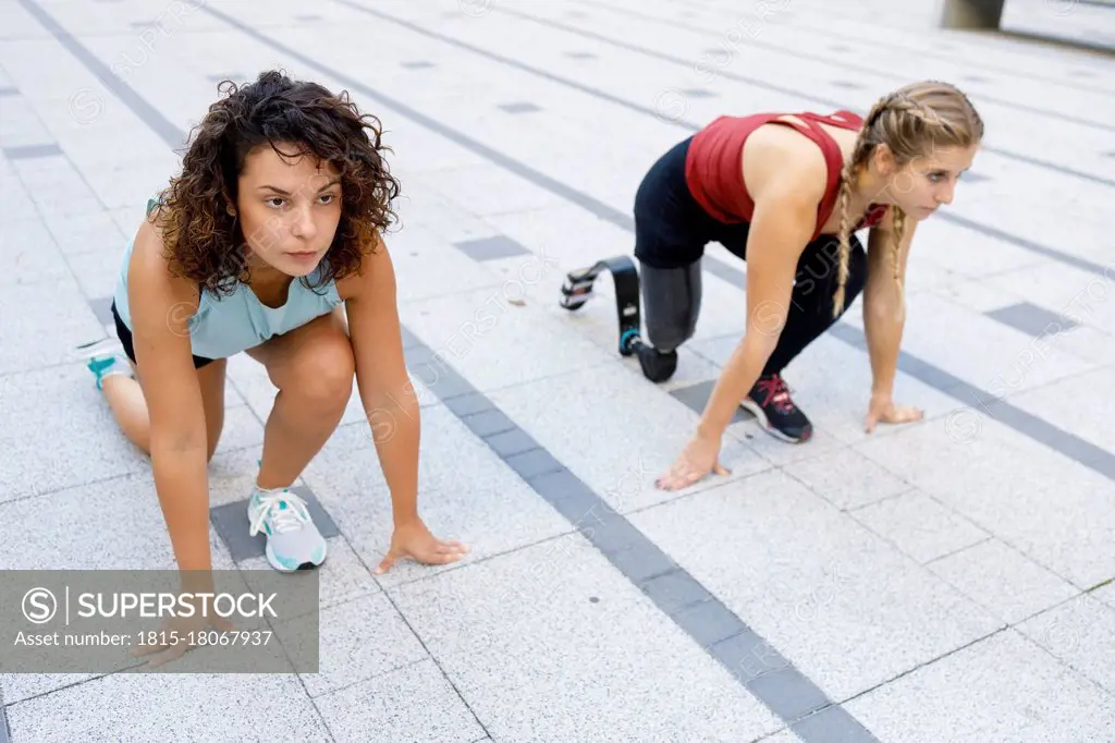 Sportswoman crouching by amputee for sports race on footpath