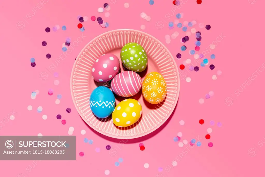 Colorful hand colored Easter eggs in tray with confetti on pink background