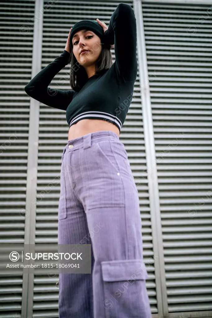 Confident young woman with hands behind head against metallic shutter