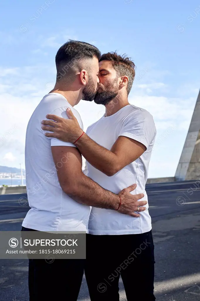 Affectionate gay couple kissing on bridge against sky