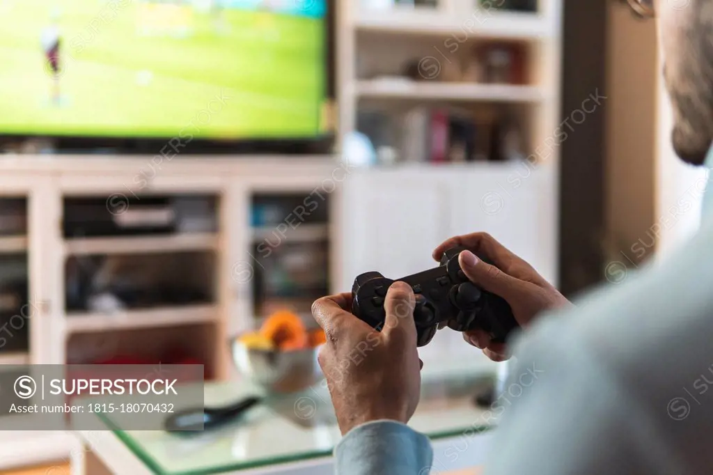 Young male gamer playing video game at home