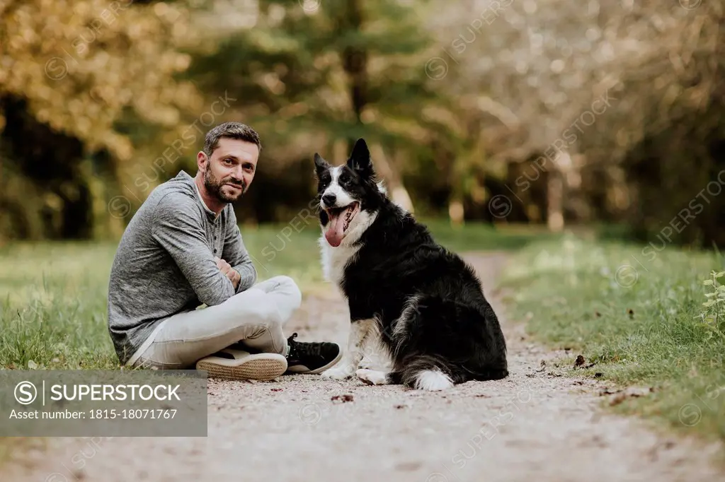 Smiling man and dog sitting on footpath at public park