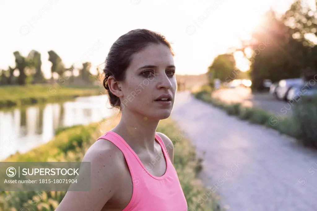 Confident sportswoman looking away while standing in park during sunset