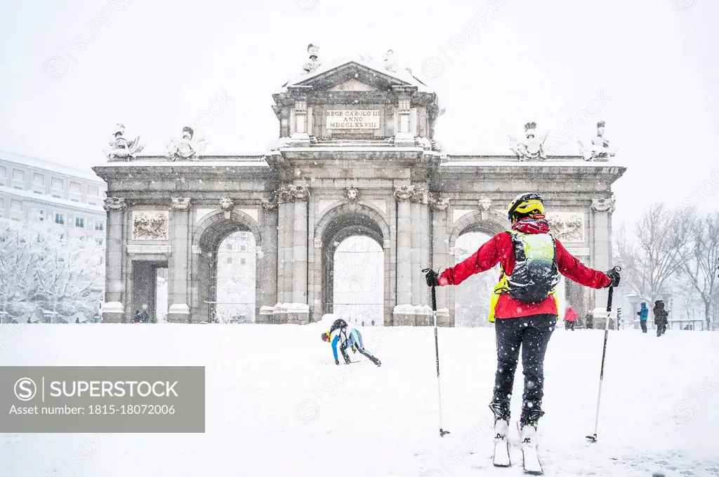Man and woman skiing on snow against Alcala Gate during Storm Filomena in 2021 at Madrid, Spain