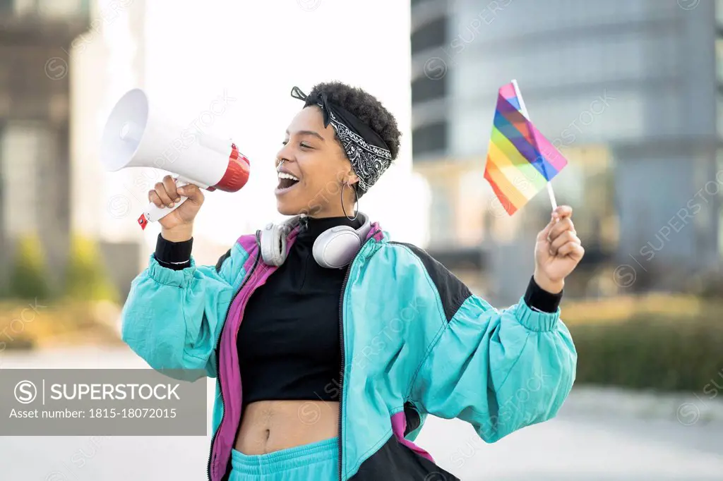 Female LGBTQIA protestor holding rainbow flag while announcing through megaphone