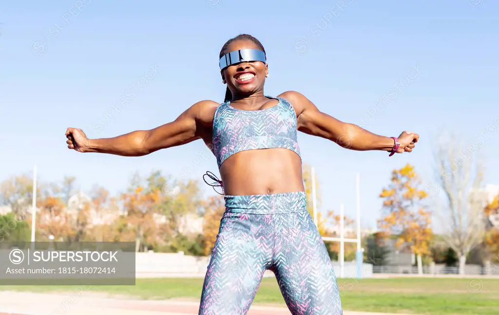 Cheerful female athlete in sunglasses jumping against clear sky on sunny day