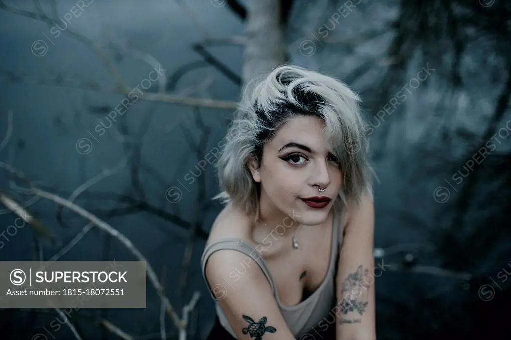 Beautiful blond woman sitting on fallen tree against lake