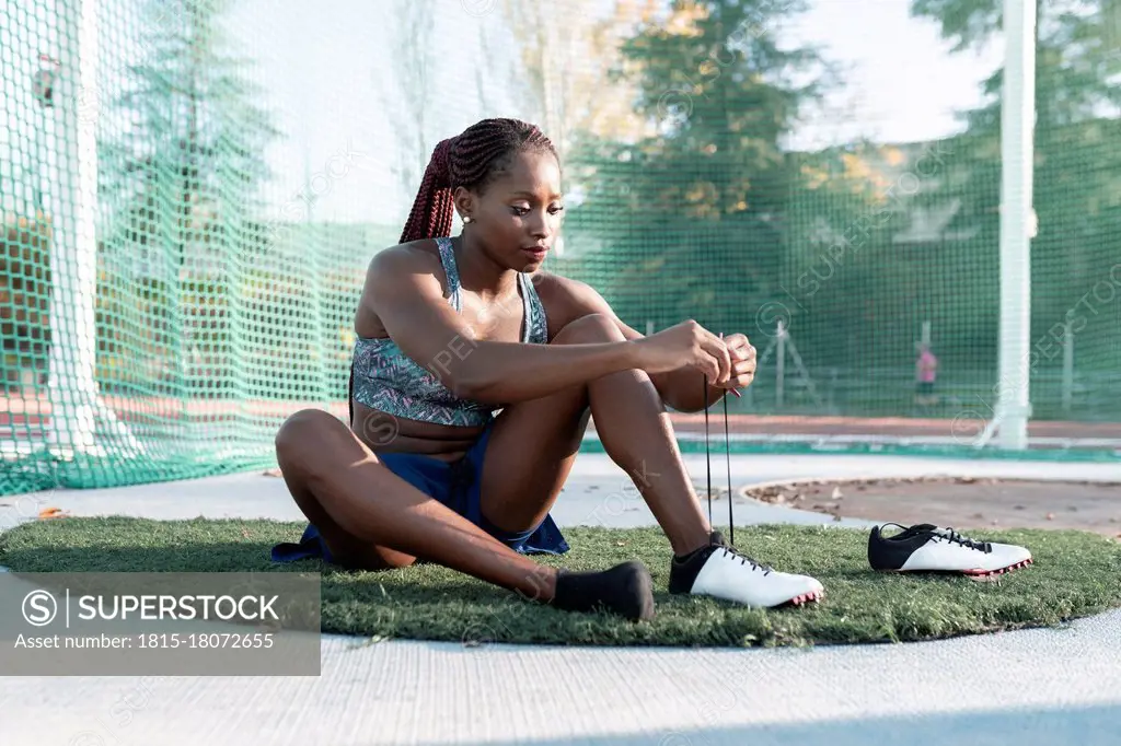 Female athlete tying shoelace against net in sports court