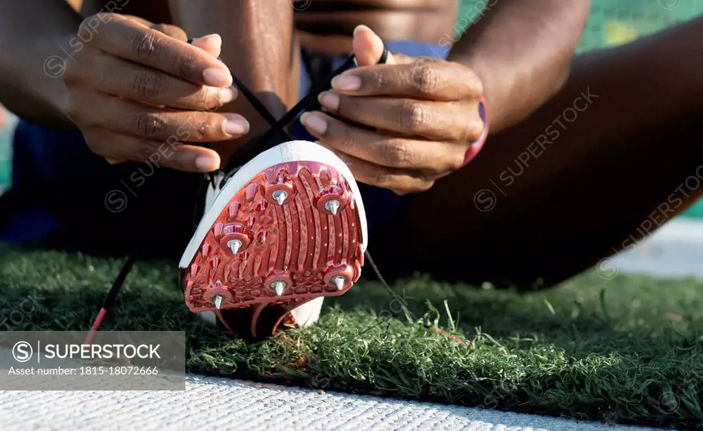 Sportswoman tying shoelace of spikes running shoes in sports court