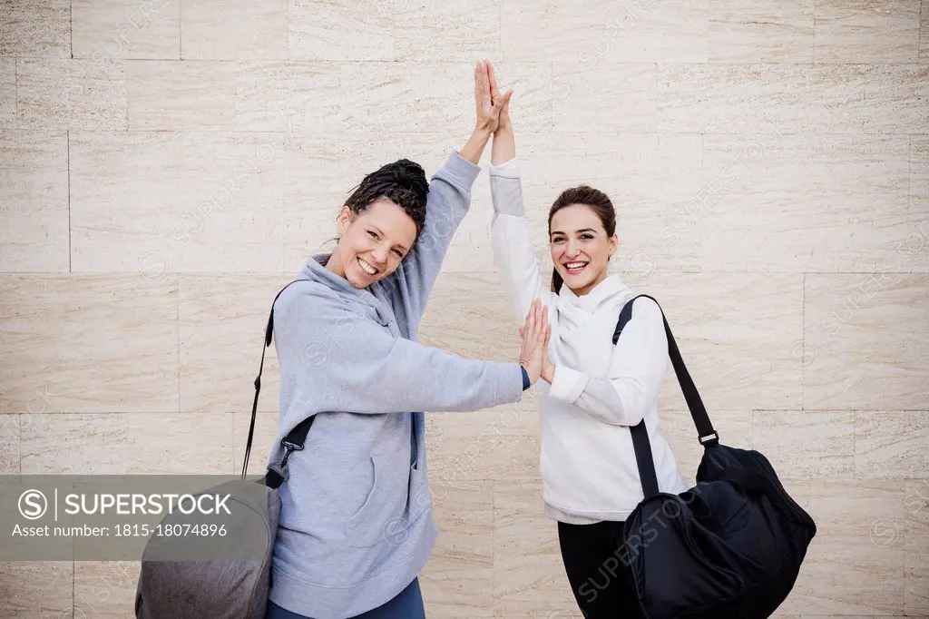 Smiling female sports people with hands clasped standing by wall