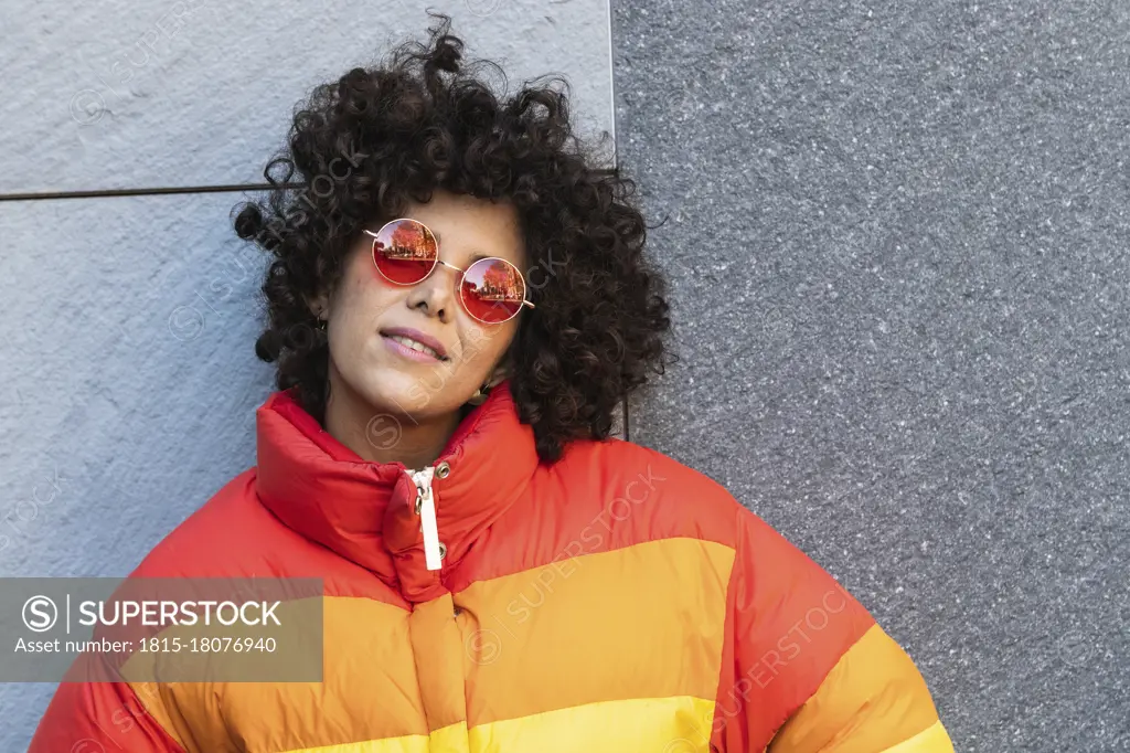 Young woman wearing sunglasses smiling while leaning on wall