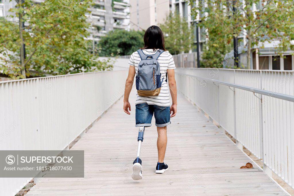 Amputed man with backpack walking on bridge in city - SuperStock