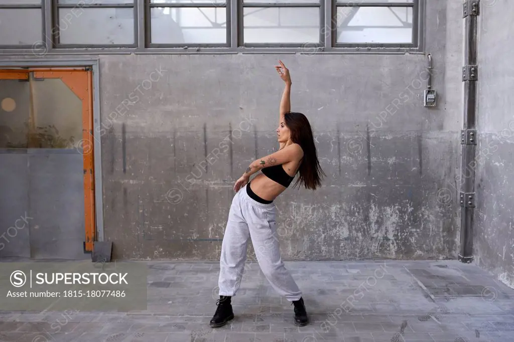 Female dancer dancing with arm raised against gray wall in abandoned factory