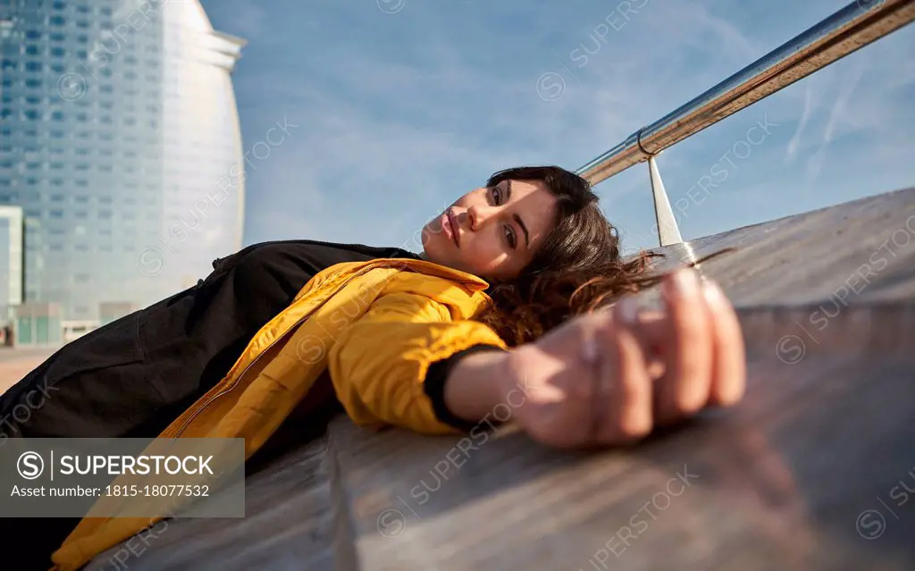 Carefree woman lying on retaining wall at pier during sunny day