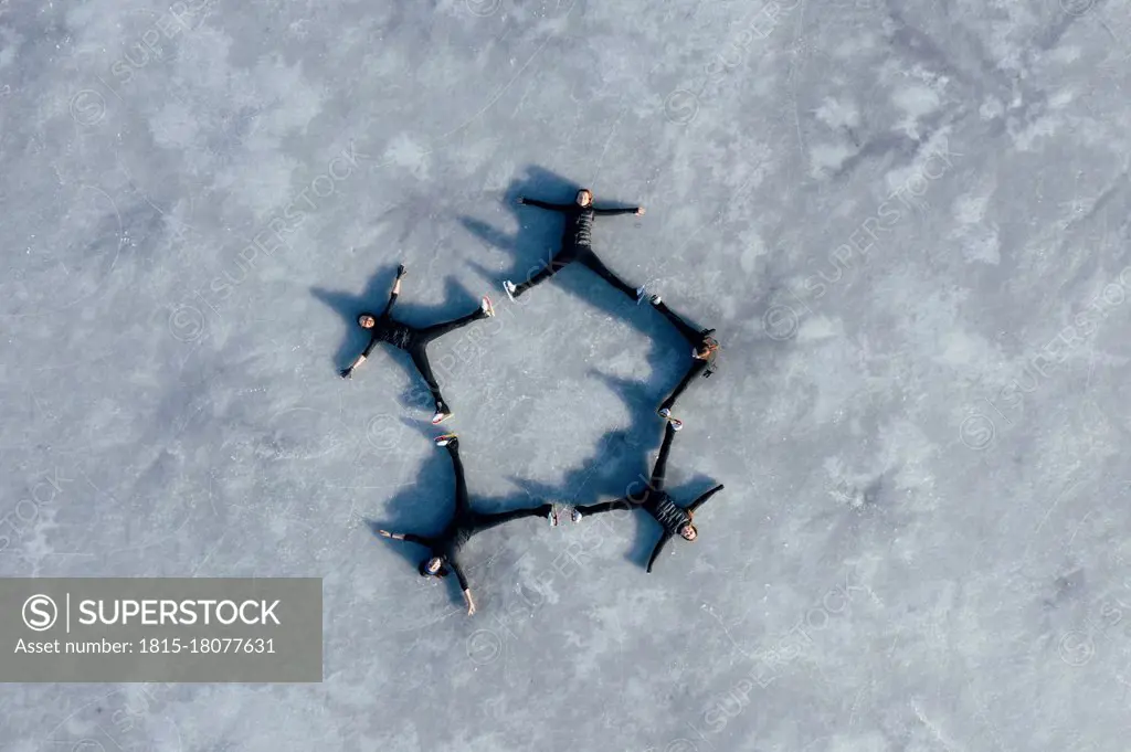 Aerial view of group of female ice-skaters lying together on surface of frozen lake