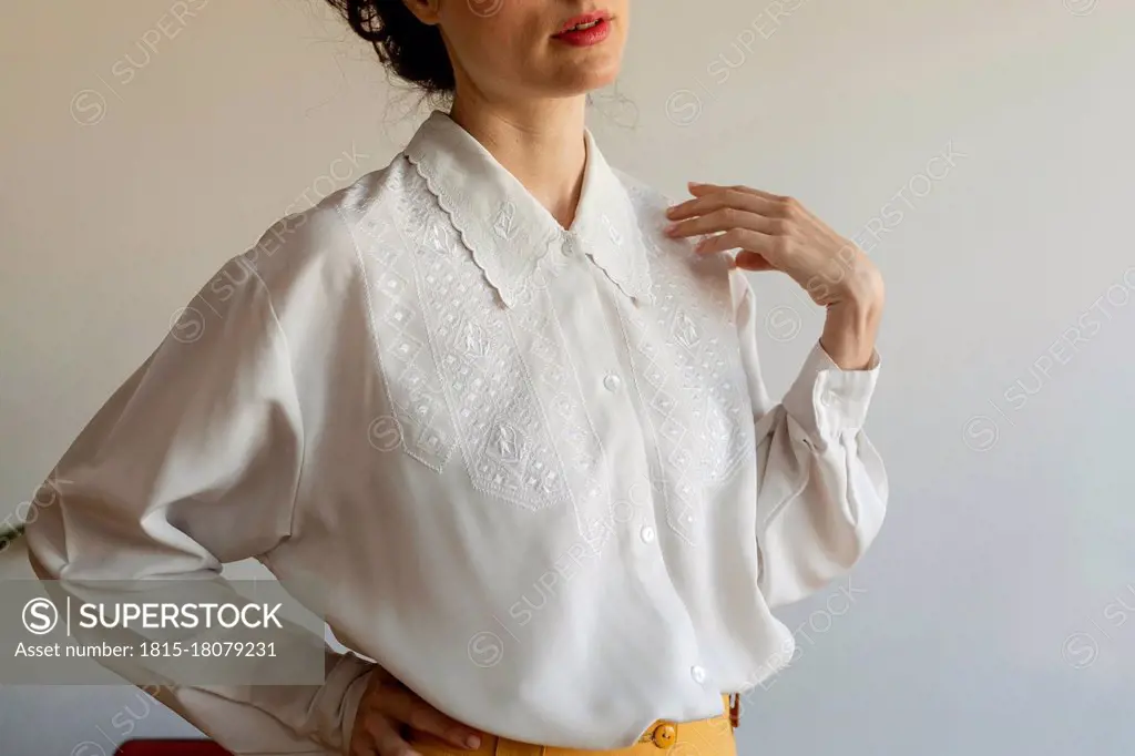 Woman wearing white shirt with hand on hip standing against wall