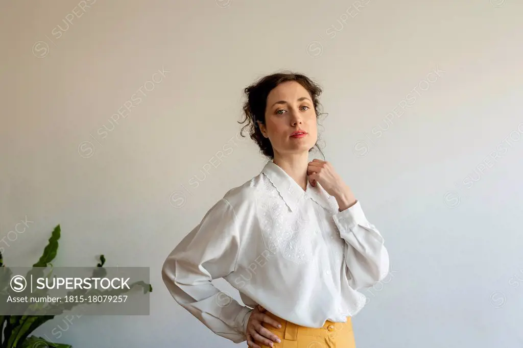 Beautiful female model with hand on hip wearing retro style clothes standing against wall