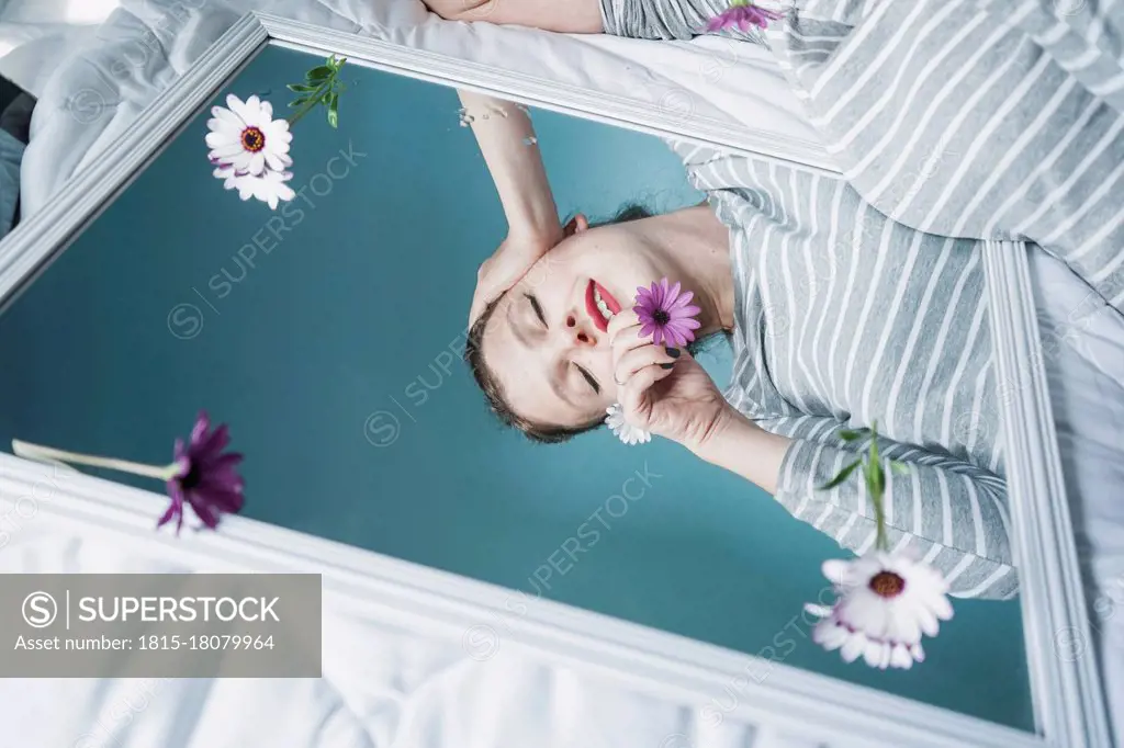 Young woman reflecting in mirror lying on bed