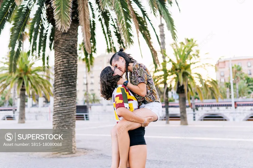 Young woman carrying girlfriend and kissing on street in city