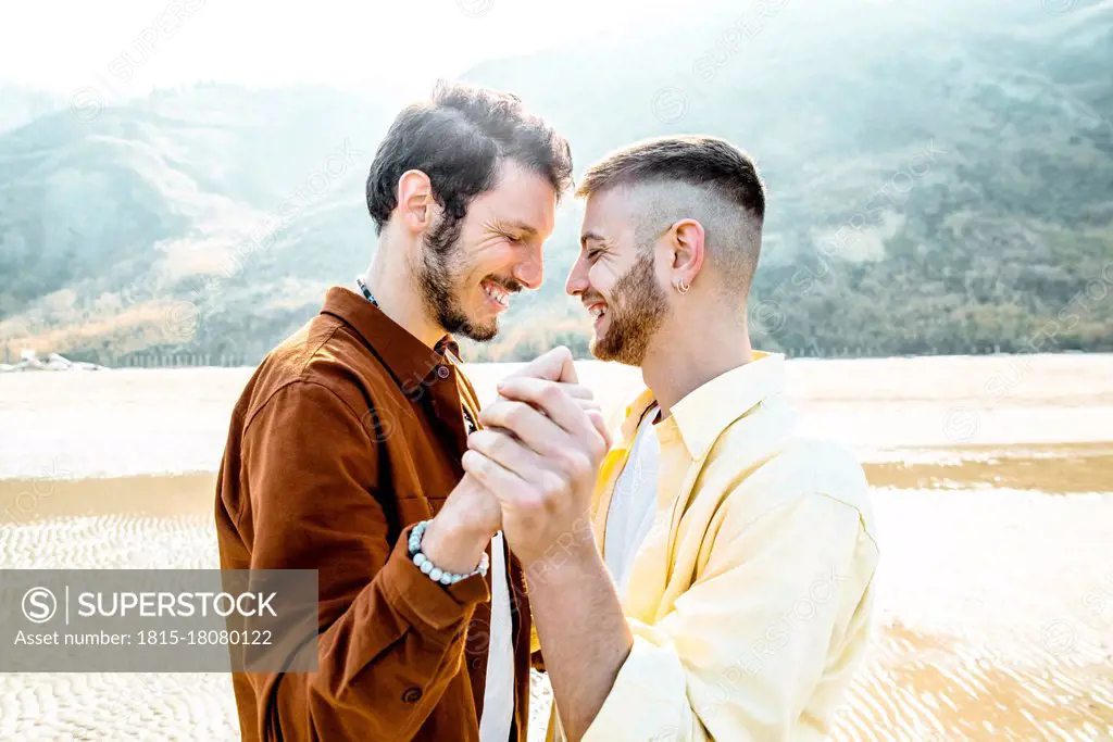 Happy gay couple with eyes closed standing at beach during vacations