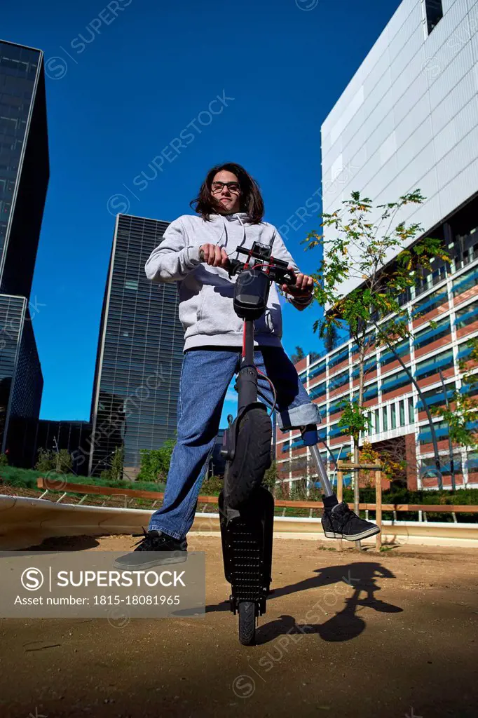 Young disabled man practicing stunt on electric push scooter in playground against buildings in city