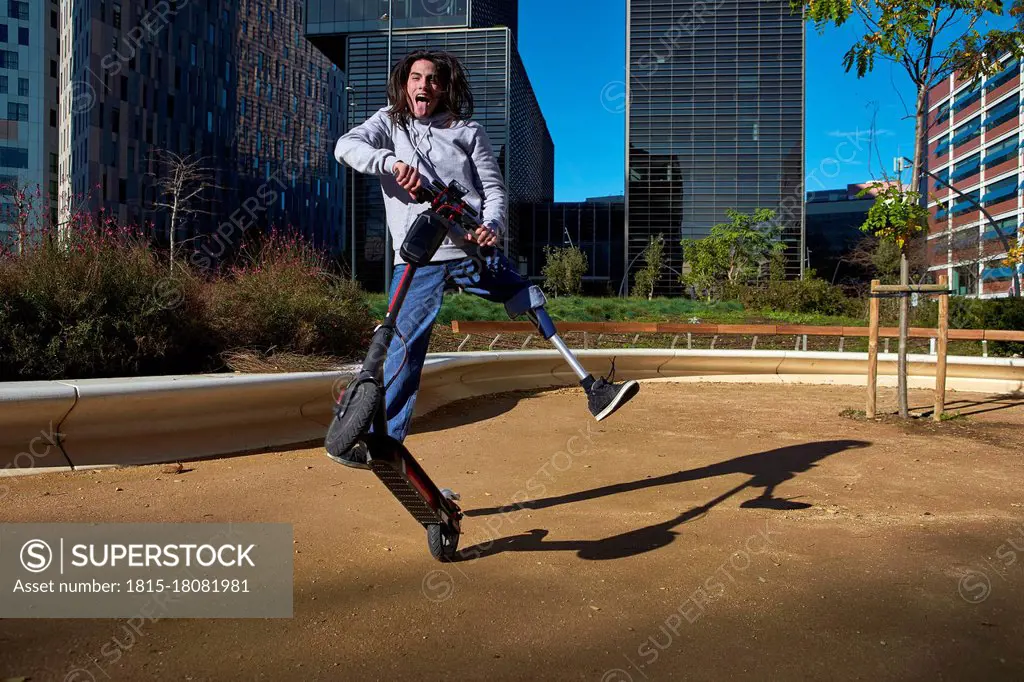 Playful disabled man practicing stunt on electric push scooter in playground against buildings in city