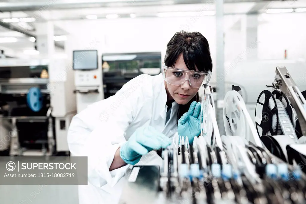 Mature female technician examining machinery in bright industry