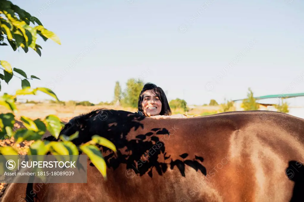 Smiling woman standing behind horse during sunny day