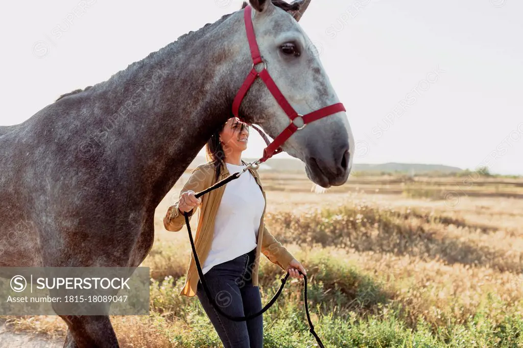 Woman holding horse bridle against meadow